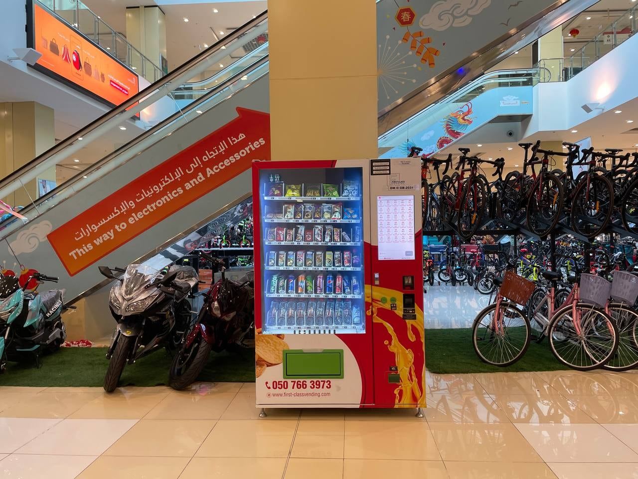 A Wendor machine near bikes and an escalator in a Dubai mall