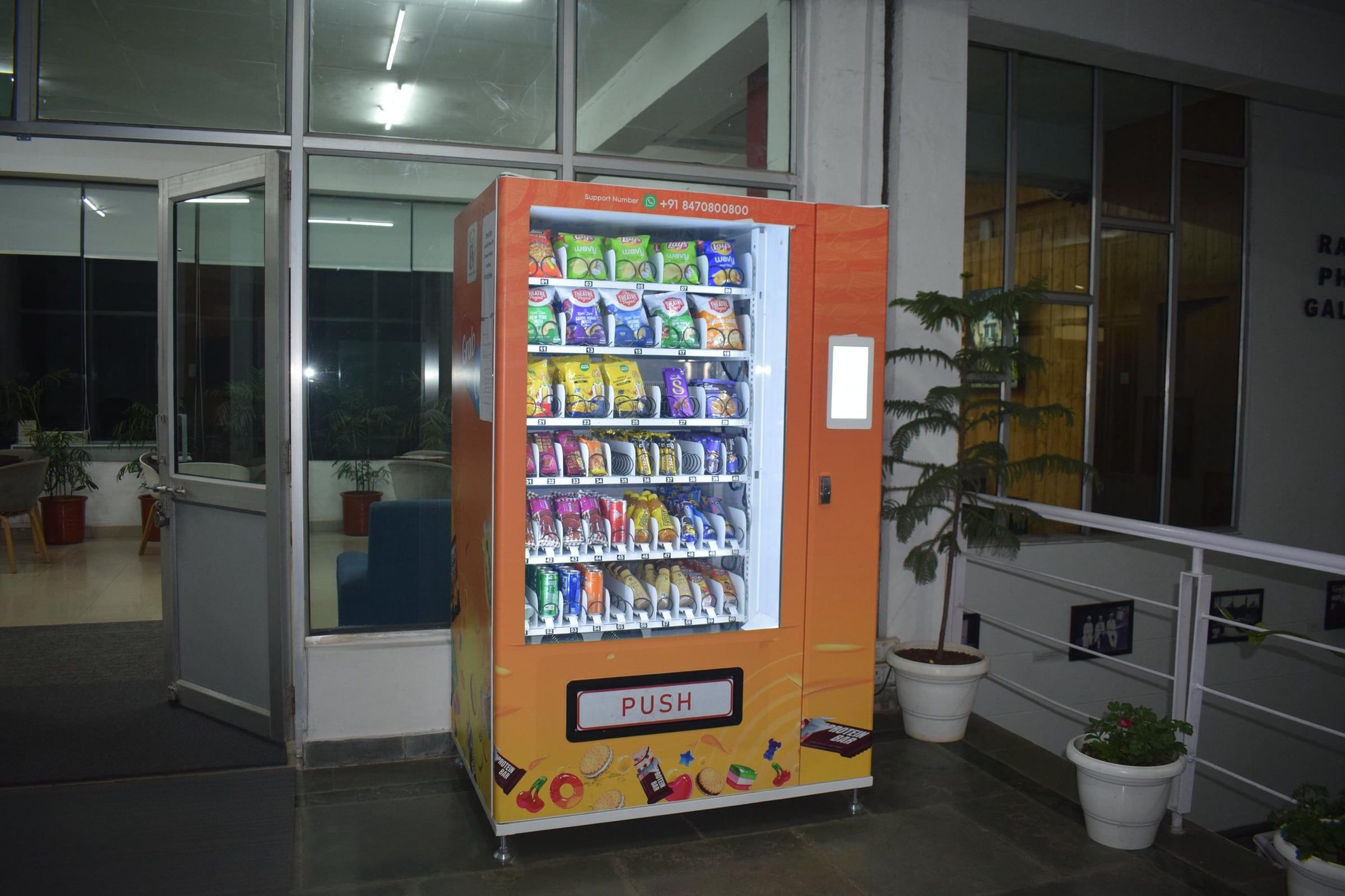 A Wendor machine outside a glass hall at night