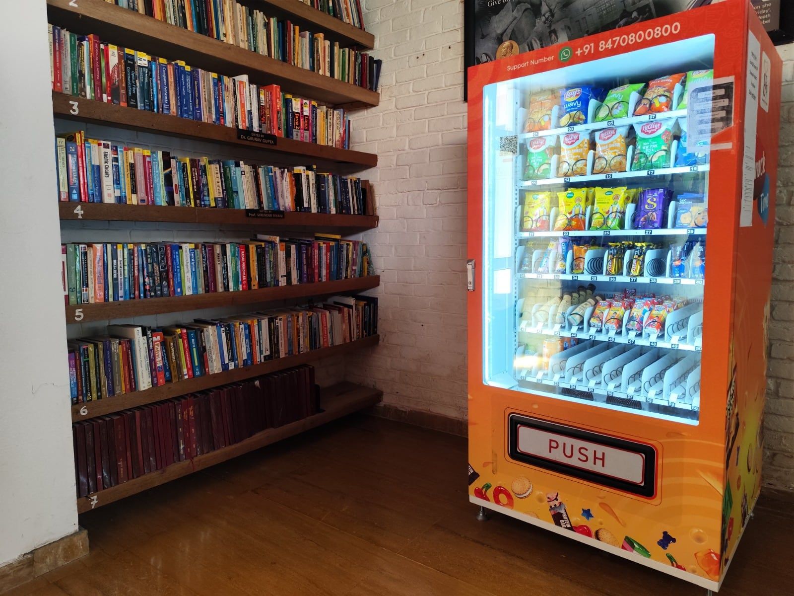 An orange Wendor machine beside library bookshelves